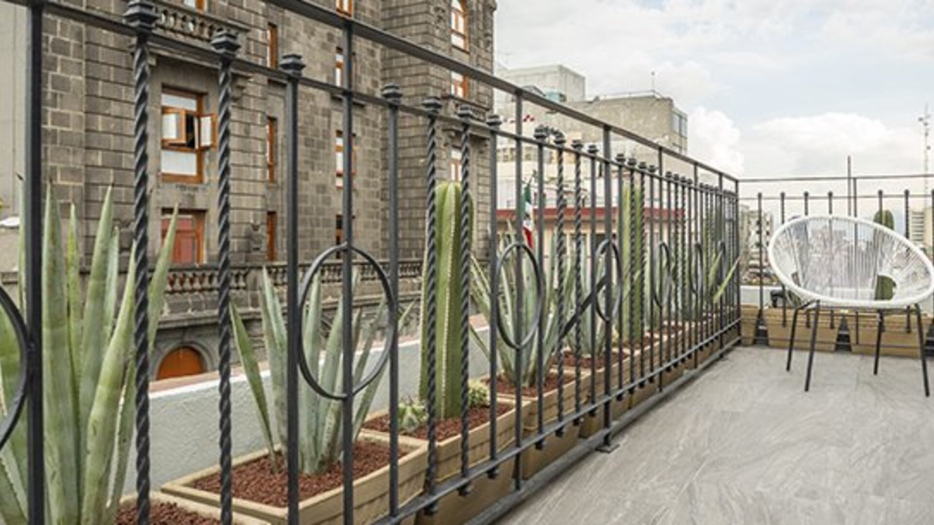 Rooftop terrace with decorative metal railings, potted succulents and a white woven chair at Hotel Principal.