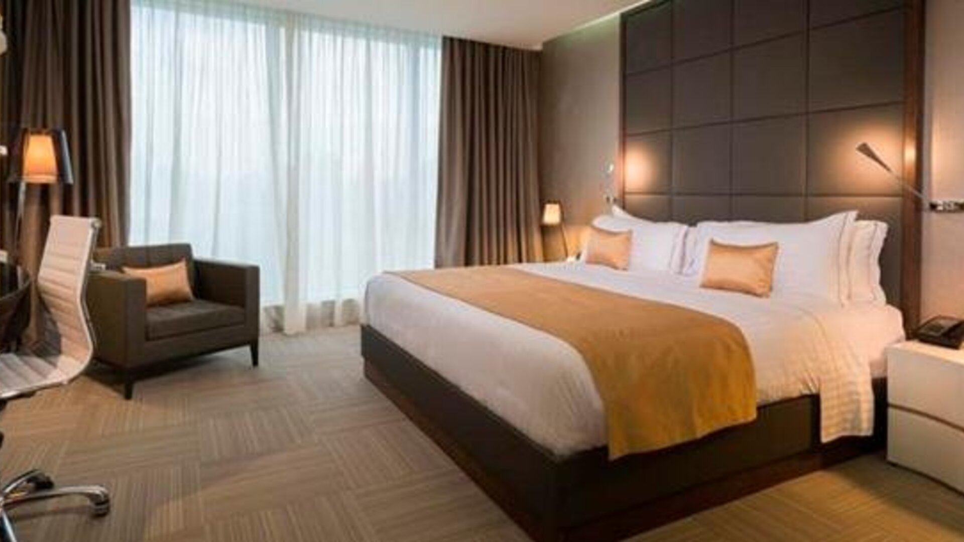 Guest bedroom with a king-size bed, gold accent cushions, bedside lighting, a desk and floor-to-ceiling windows at Hotel Las Américas Golden Tower Panamá.