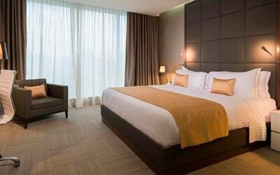 Guest bedroom with a king-size bed, gold accent cushions, bedside lighting, a desk and floor-to-ceiling windows at Hotel Las Américas Golden Tower Panamá.