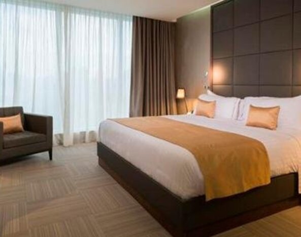 Guest bedroom with a king-size bed, gold accent cushions, bedside lighting, a desk and floor-to-ceiling windows at Hotel Las Américas Golden Tower Panamá.