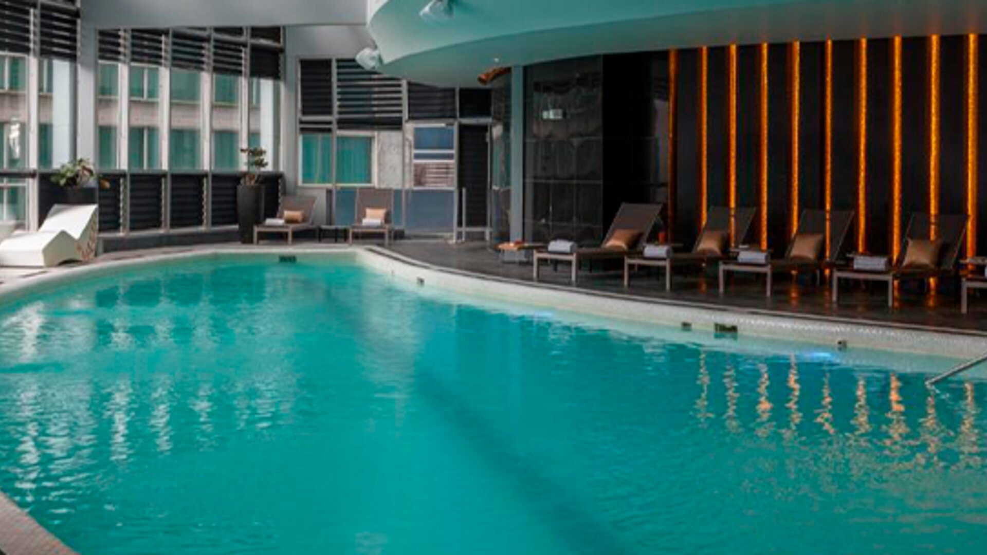 Indoor swimming pool with turquoise water, loungers and floor-to-ceiling windows at Hotel Las Américas Golden Tower Panamá.
