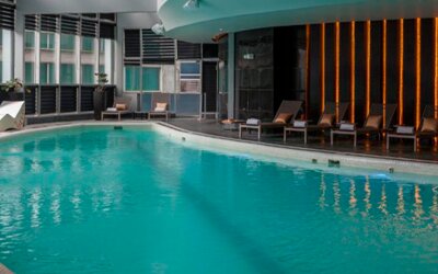 Indoor swimming pool with turquoise water, loungers and floor-to-ceiling windows at Hotel Las Américas Golden Tower Panamá.