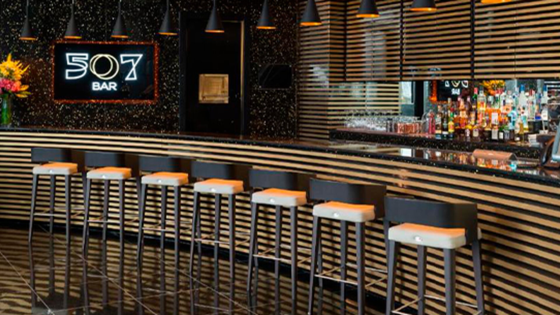 Bar 507 with a long counter, striped decorative panels, pendant lighting and bar stools at Hotel Las Américas Golden Tower Panamá.