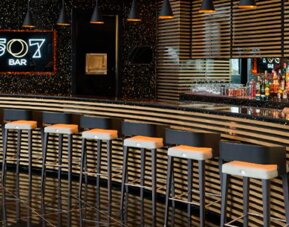 Bar 507 with a long counter, striped decorative panels, pendant lighting and bar stools at Hotel Las Américas Golden Tower Panamá.