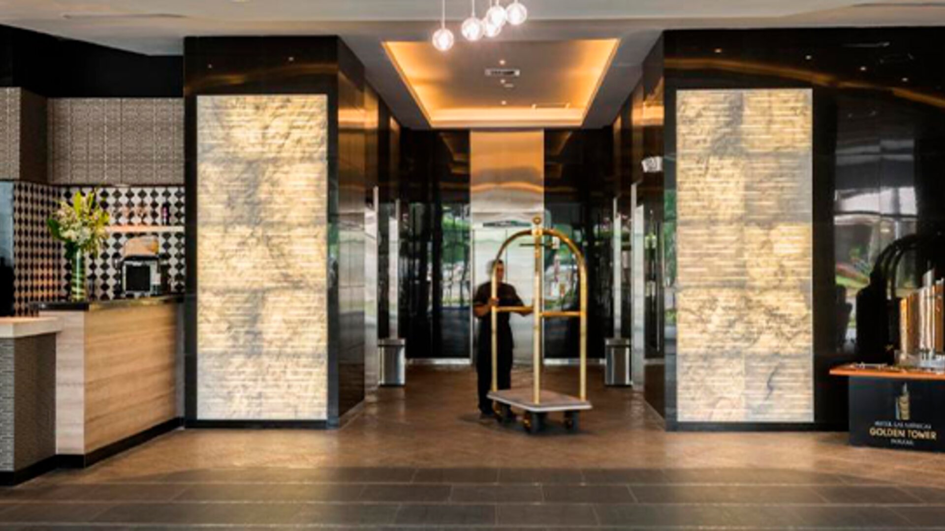 Hotel lobby entrance with illuminated stone columns, polished flooring and a luggage trolley at Hotel Las Américas Golden Tower Panamá.