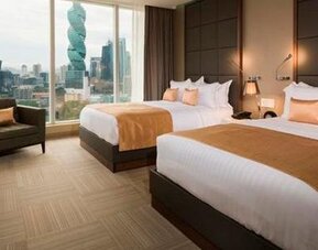Guest room with two double beds, gold accent cushions, an armchair and city views through large windows at Hotel Las Américas Golden Tower Panamá.