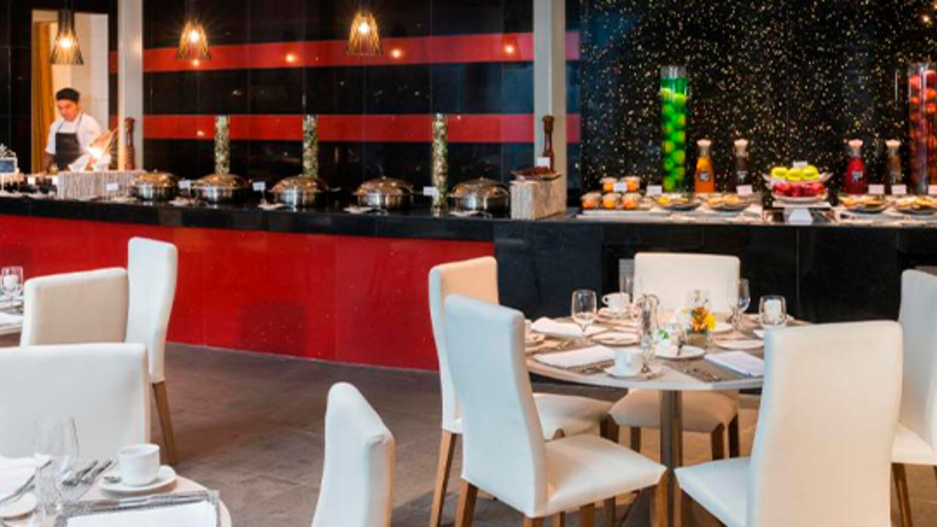 Restaurant dining area with white upholstered chairs, set tables and a buffet counter at Hotel Las Américas Golden Tower Panamá.