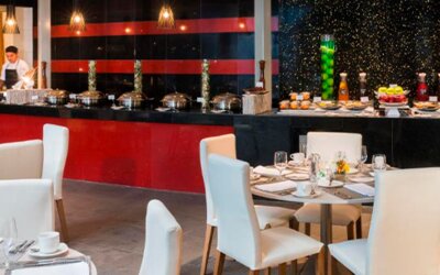 Restaurant dining area with white upholstered chairs, set tables and a buffet counter at Hotel Las Américas Golden Tower Panamá.
