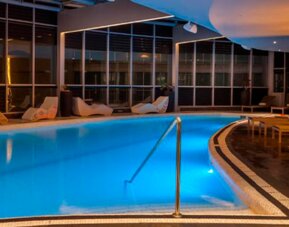 Indoor swimming pool with turquoise water, surrounding loungers and warm ambient lighting at Hotel Las Américas Golden Tower Panamá.