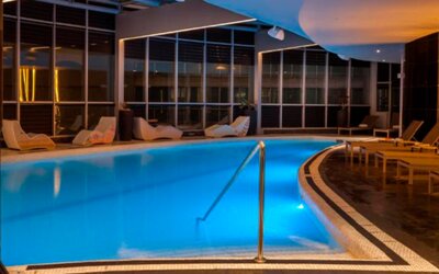 Indoor swimming pool with turquoise water, surrounding loungers and warm ambient lighting at Hotel Las Américas Golden Tower Panamá.