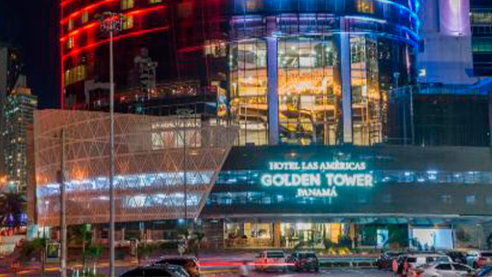 Night-time exterior of Hotel Las Américas Golden Tower Panamá, featuring illuminated glass architecture and colourful building lights.