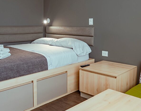 Compact studio with a bed, light wood furniture, upholstered headboard and a green accent chair with a patterned cushion at UMA Suites Chía.