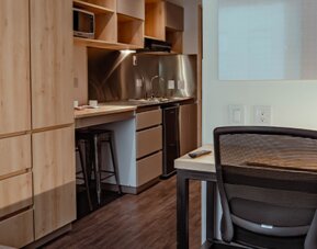 Studio interior with wooden cabinetry, a compact kitchenette, desk, office chair and dark wood-effect flooring at UMA Suites Chía.