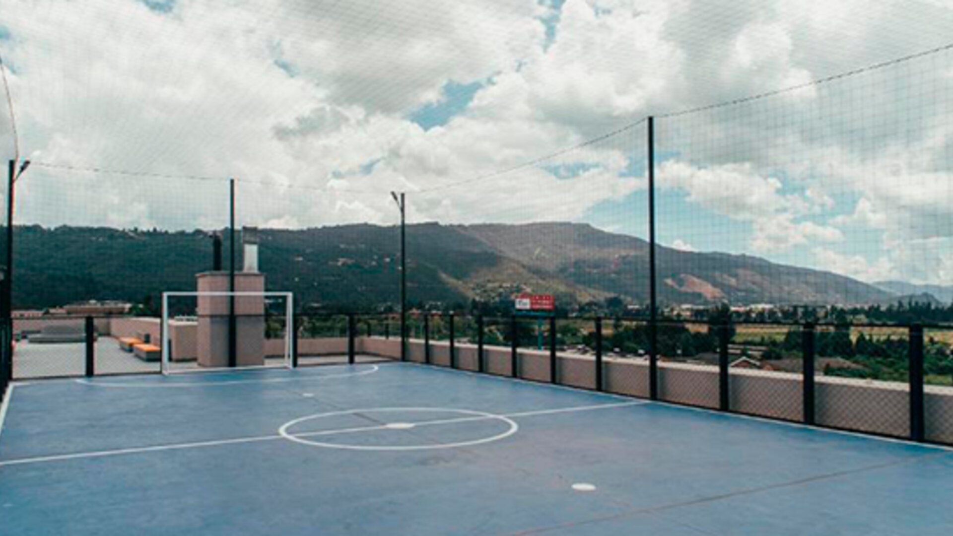 Rooftop sports court with blue flooring, basketball markings, safety netting and mountain views at UMA Suites Chía.