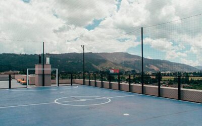 Rooftop sports court with blue flooring, basketball markings, safety netting and mountain views at UMA Suites Chía.