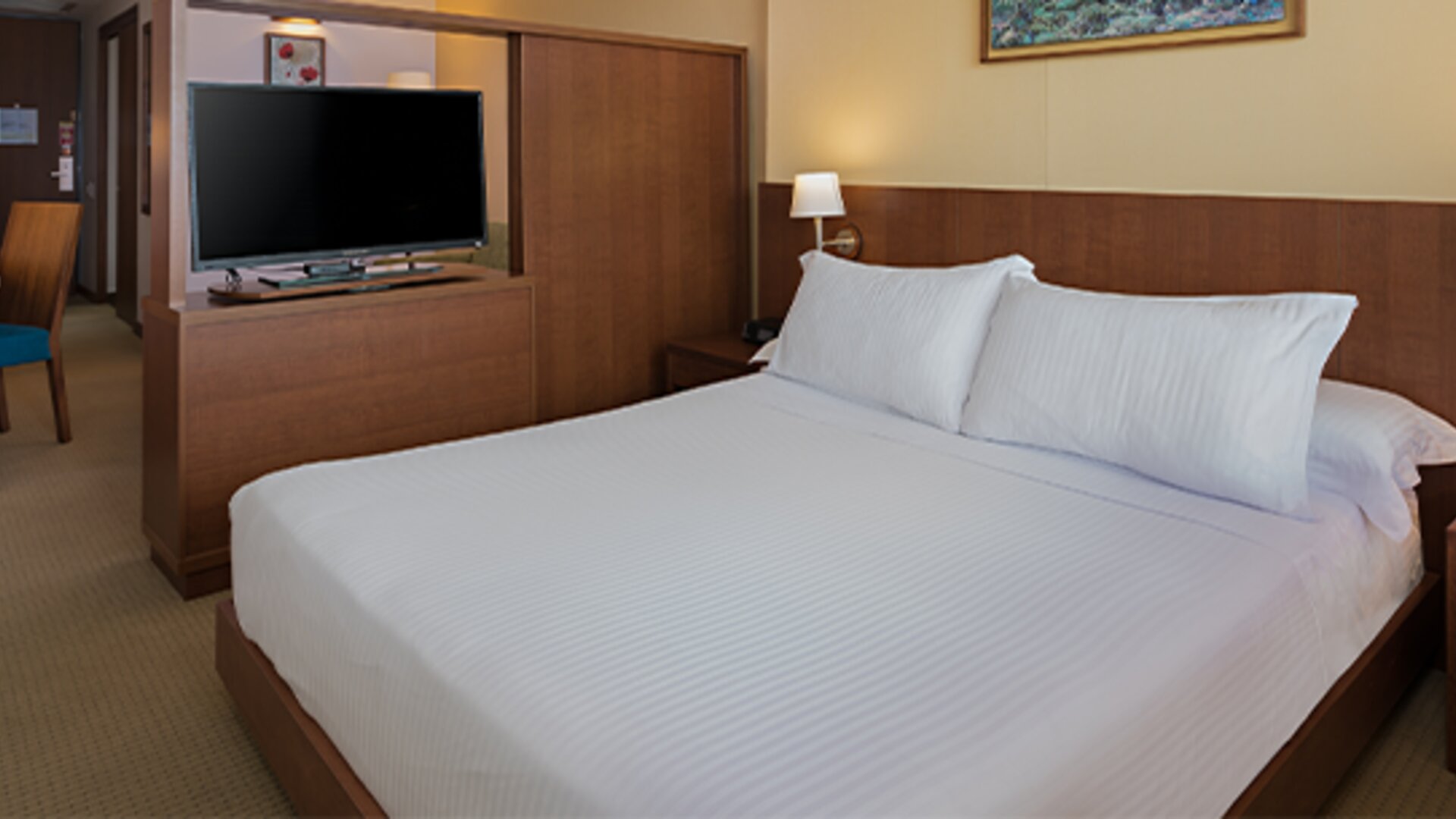 1. King guest room with white bedding, a wooden headboard, bedside tables, wall-mounted lamps and a television at Hotel Habitel Select.