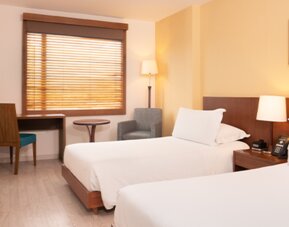 Twin guest room with white bedding, wooden bed frames, a desk, television and window blinds at Hotel Habitel Select.