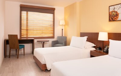 Twin guest room with white bedding, wooden bed frames, a desk, television and window blinds at Hotel Habitel Select.