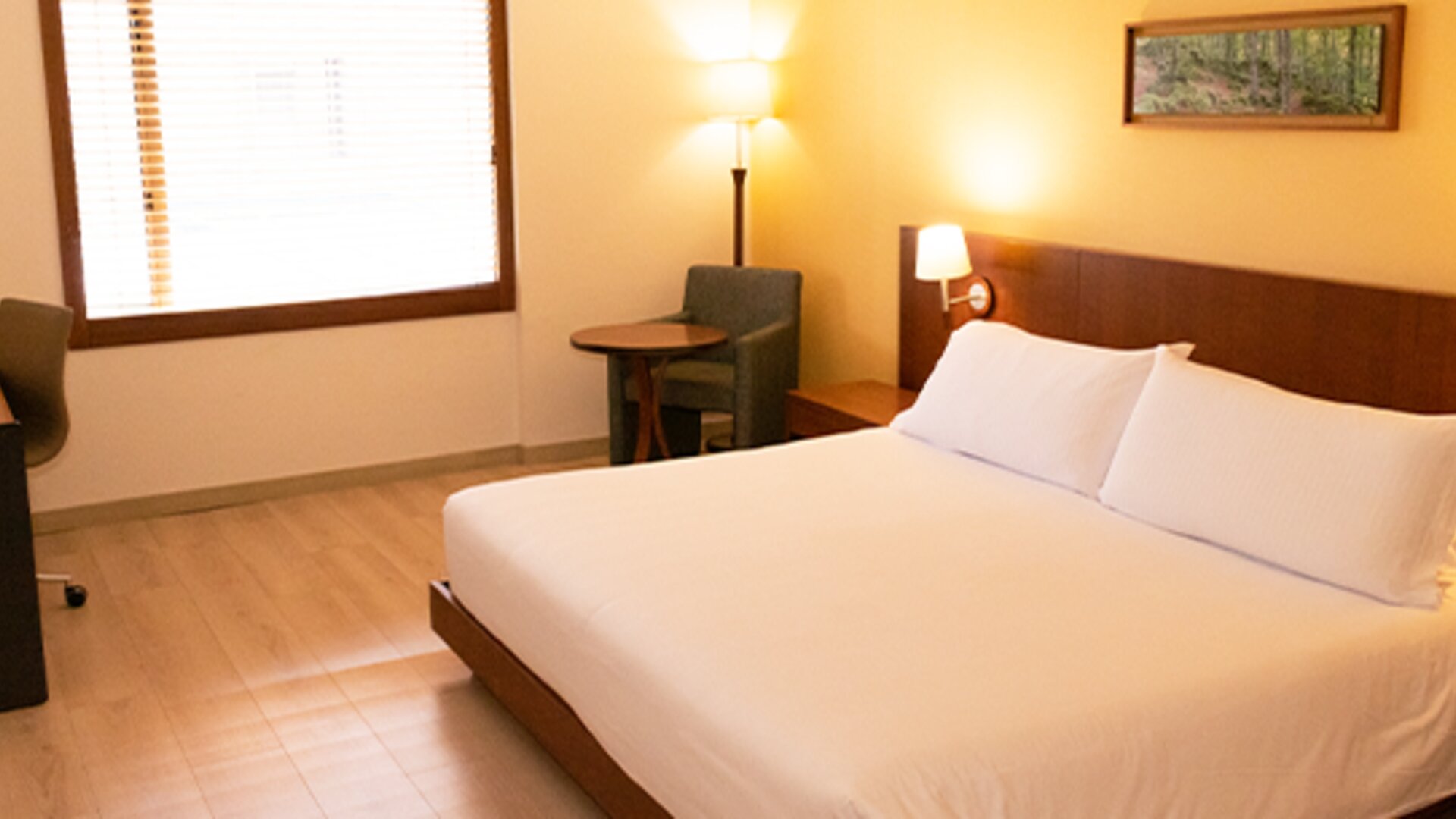 Guest bedroom with a large double bed, white bedding, wooden headboard, bedside lamps and a small seating area at Hotel Habitel Select.