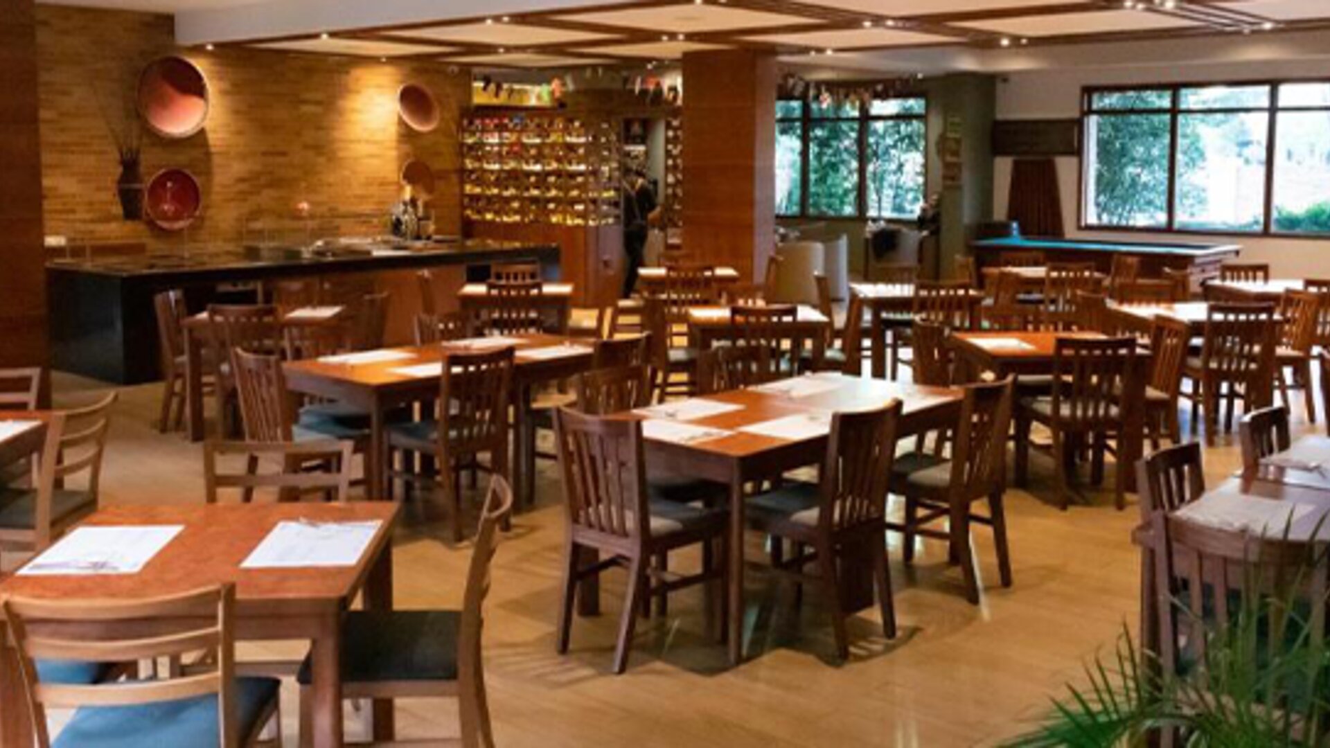 Restaurant dining area with wooden tables and chairs, warm lighting, decorative wine storage and large windows at Hotel Habitel Select.