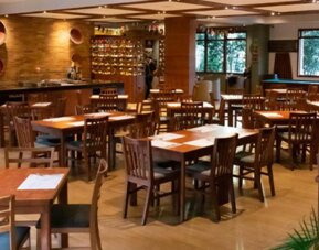 Restaurant dining area with wooden tables and chairs, warm lighting, decorative wine storage and large windows at Hotel Habitel Select.