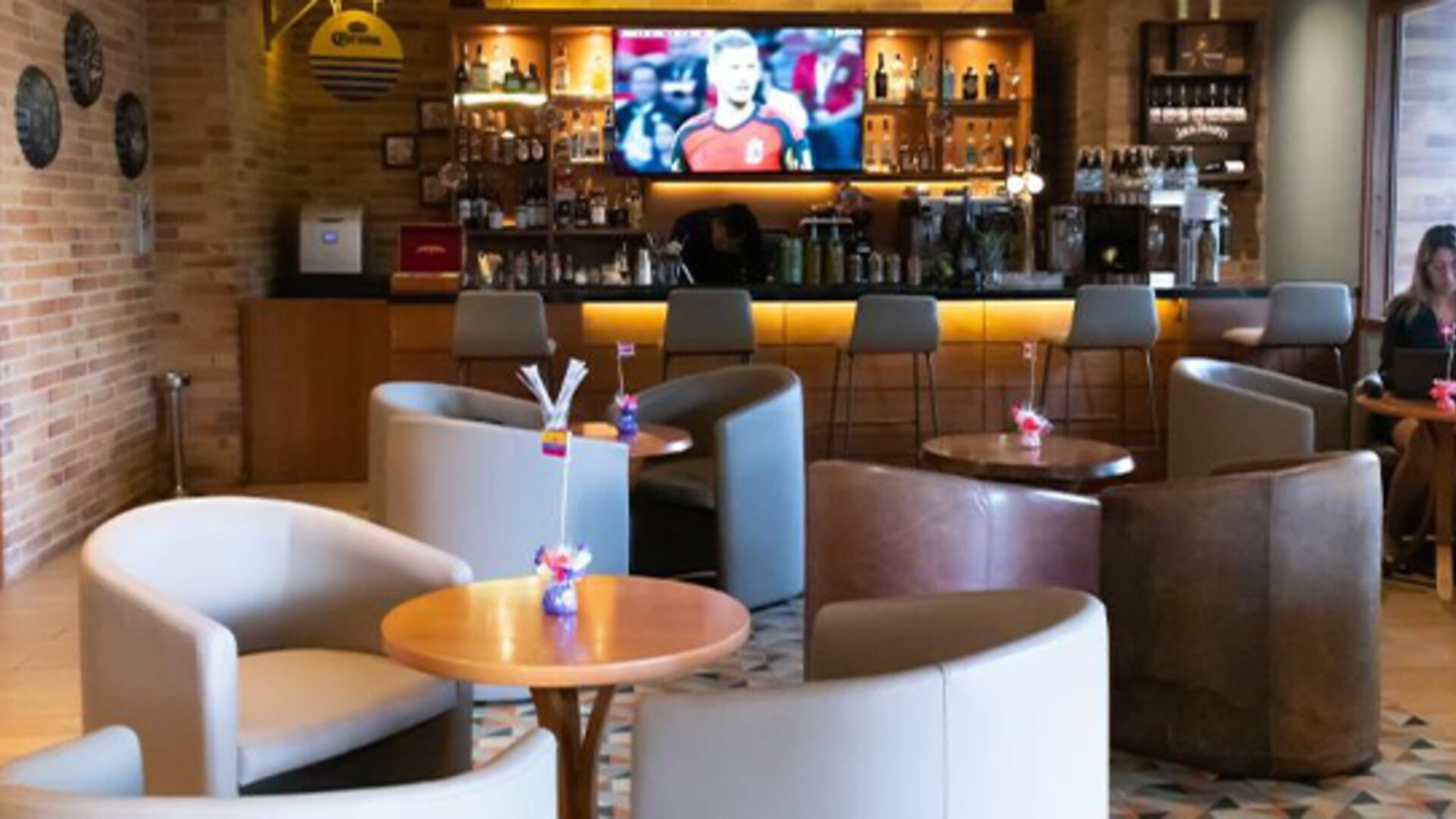 Hotel bar and lounge with upholstered armchairs, round coffee tables, a wooden bar counter and a television at Hotel Habitel Select.