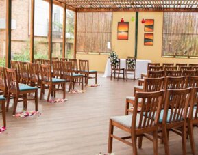 Outdoor dining or event space with rows of wooden chairs, a slatted timber canopy and surrounding greenery at Hotel Habitel Select.