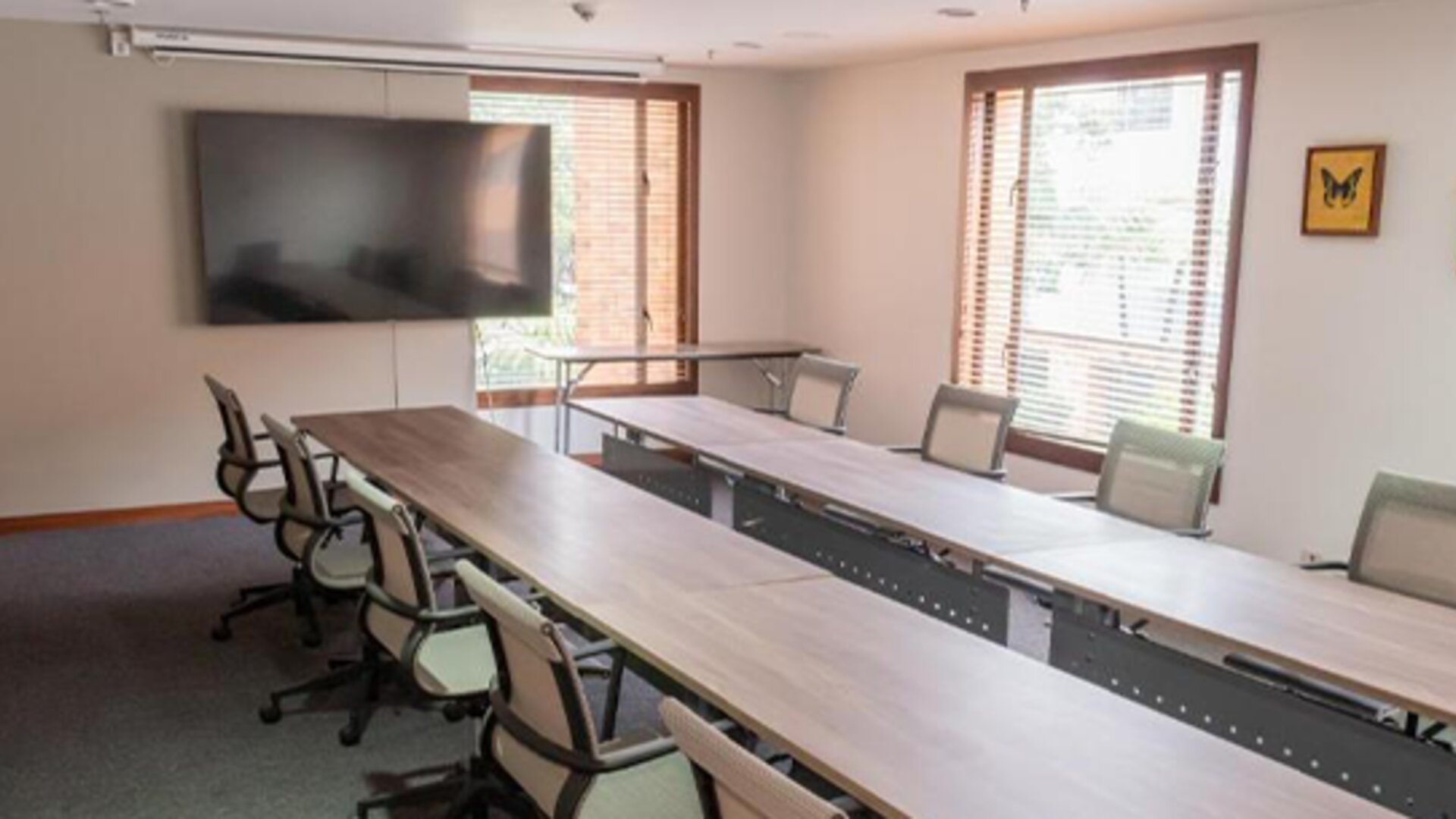 Meeting room with a long conference table, office chairs, large windows and a wall-mounted television at Hotel Habitel Select.