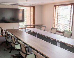 Meeting room with a long conference table, office chairs, large windows and a wall-mounted television at Hotel Habitel Select.