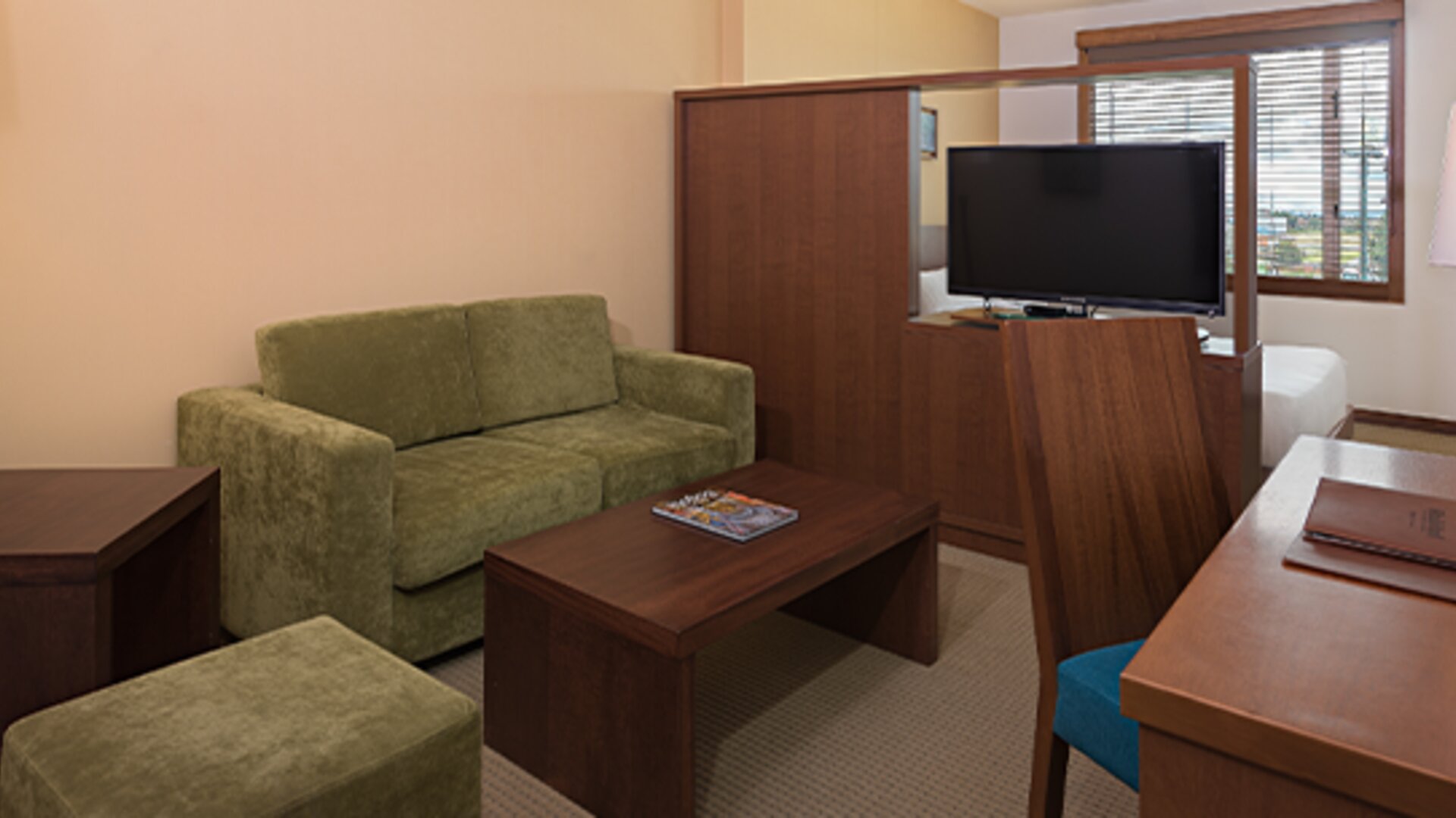 Guest suite lounge with a green sofa, wooden coffee table, television, desk and warm wood furnishings at Hotel Habitel Select.