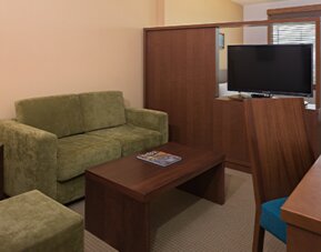 Guest suite lounge with a green sofa, wooden coffee table, television, desk and warm wood furnishings at Hotel Habitel Select.