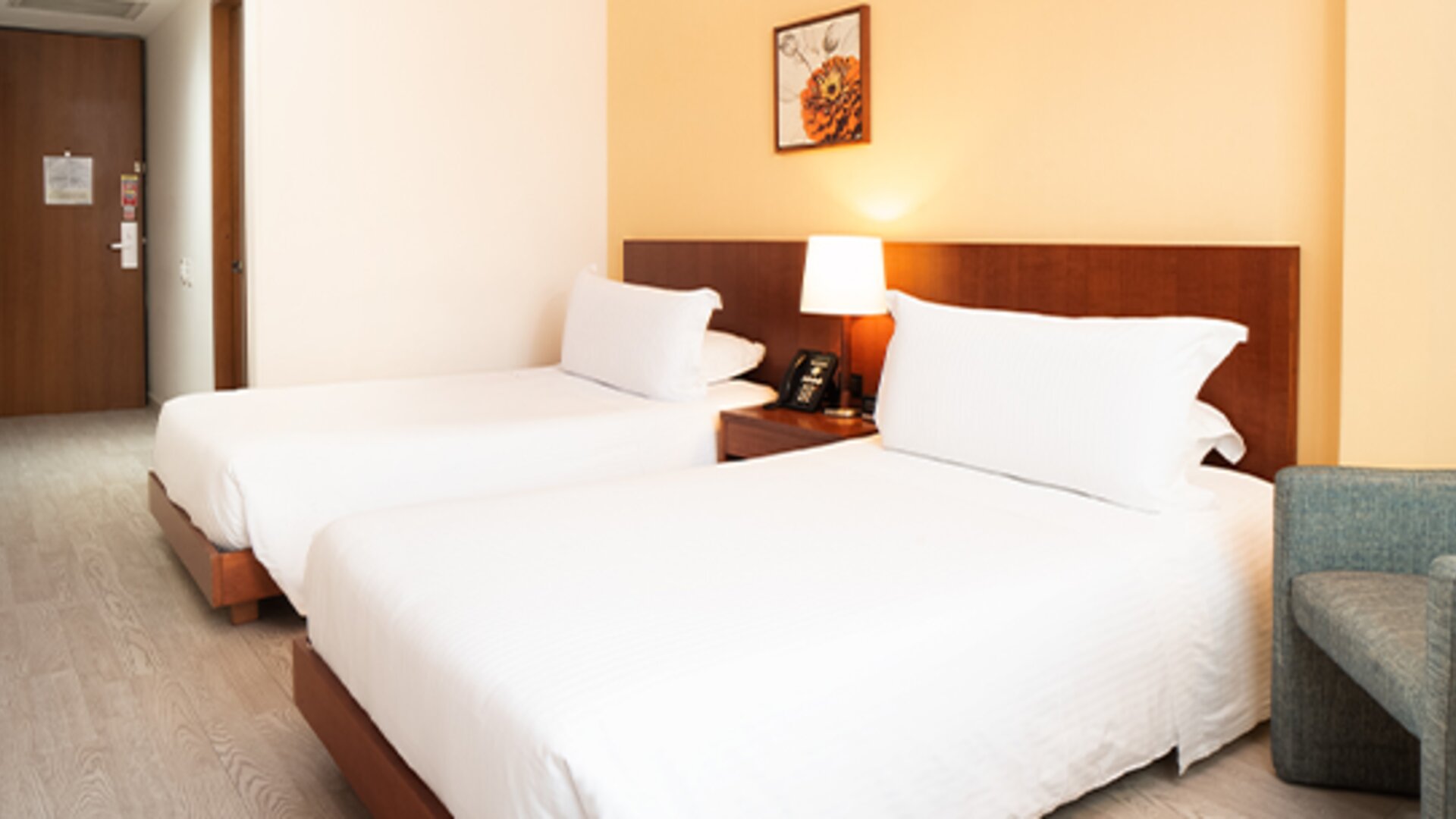 Twin guest room with two single beds, white bedding, wooden headboards, bedside lighting and a blue upholstered armchair at Hotel Habitel Select.