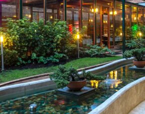 Curved ornamental pond with water fountains, planted greenery and outdoor lighting beside the hotel at Hotel Habitel Select.