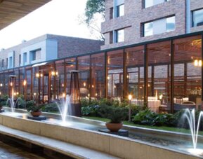 Landscaped hotel courtyard with a long water feature, fountains, potted plants and a glass-fronted building at Hotel Habitel Select.