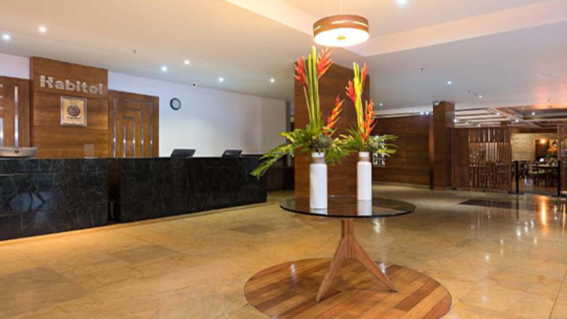Hotel reception with a dark marble front desk, wooden wall panels, floral arrangements and polished stone flooring at Hotel Habitel Select.
