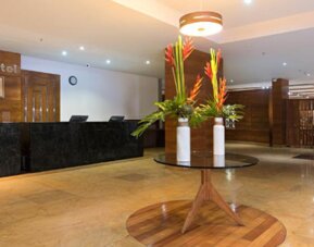 Hotel reception with a dark marble front desk, wooden wall panels, floral arrangements and polished stone flooring at Hotel Habitel Select.
