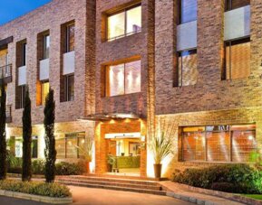 Brick hotel exterior illuminated at dusk, with landscaped gardens, tall windows and a warmly lit entrance at Hotel Habitel Select.