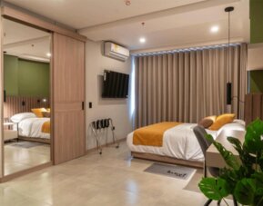 Modern guest room with a double bed, mustard accent cushions, mirrored wardrobe, wall-mounted television, and potted plant at Hotel Living 35 Suites.