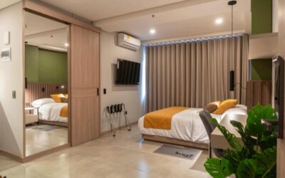 Modern guest room with a double bed, mustard accent cushions, mirrored wardrobe, wall-mounted television, and potted plant at Hotel Living 35 Suites.