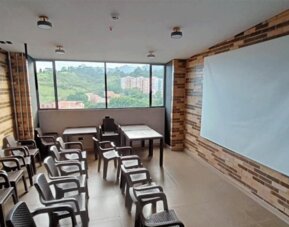 Meeting room with rows of chairs and tables, a large presentation board, exposed brick walls, and windows overlooking greenery at Hotel Living 35 Suites.