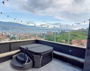 Rooftop terrace with a hot tub, built-in seating, glass railings, string lights, and panoramic city and mountain views at Hotel Living 35 Suites.