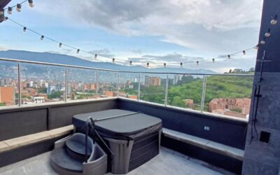 Rooftop terrace with a hot tub, built-in seating, glass railings, string lights, and panoramic city and mountain views at Hotel Living 35 Suites.