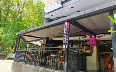 Street-level entrance with a covered terrace, black railings, vertical signage, and surrounding greenery at Hotel Living 35 Suites.