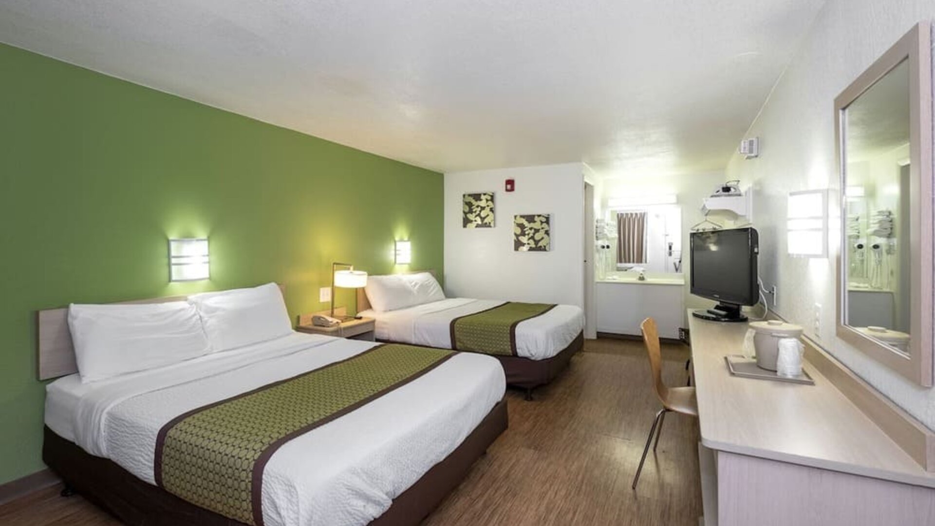 Guest room with two double beds, white bedding, green accent wall, matching bed runners, a television, and a long work desk at American Inn Carlisle.