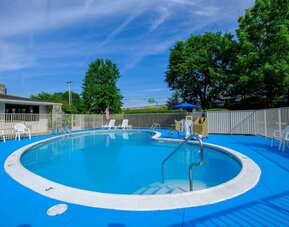 Outdoor swimming pool surrounded by a bright blue deck, white fencing, lounge chairs, and trees at American Inn Carlisle.