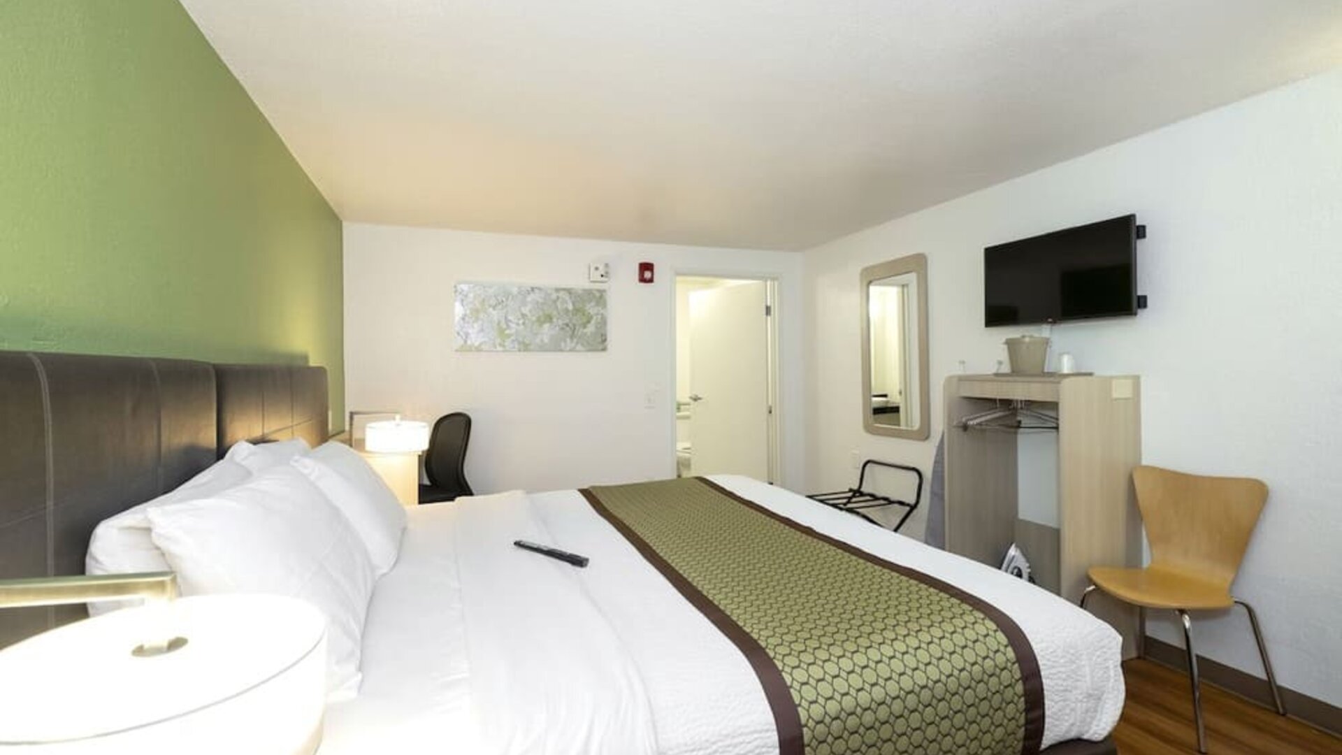 Guest room with a king-size bed, white bedding, green accent wall, bedside lamp, television, and compact work area at American Inn Carlisle.