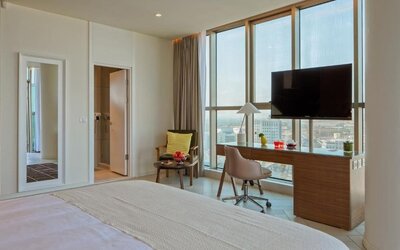 Guest room with a king-size bed, white bedding, floor-to-ceiling windows, a desk and chair, television, and a separate seating area at Prima Millennium.