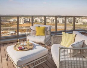 Rooftop lounge area with white cushioned outdoor sofas, yellow accent cushions, a low coffee table, and expansive city views at Prima Millennium.