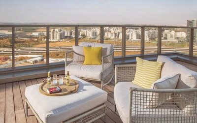 Rooftop lounge area with white cushioned outdoor sofas, yellow accent cushions, a low coffee table, and expansive city views at Prima Millennium.