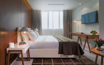 Bright guest bedroom with a king-size bed, white bedding, dark throw, wood-panelled wall, bedside table, television, and desk at Prima Millennium.